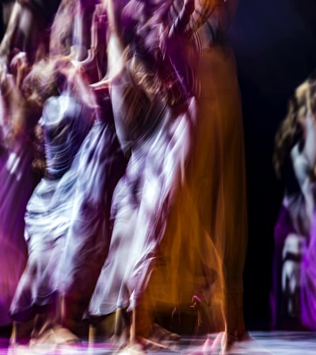 Women in long, flowy dresses, purple, orange, fuchsia - dancing ecstatically, with arms in the air.