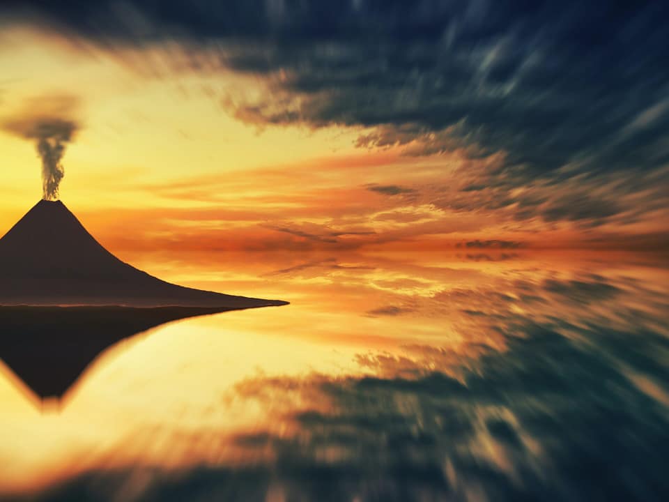 Mirror image of a volcano spurting. It's dark, and the sky is orange and yellow.