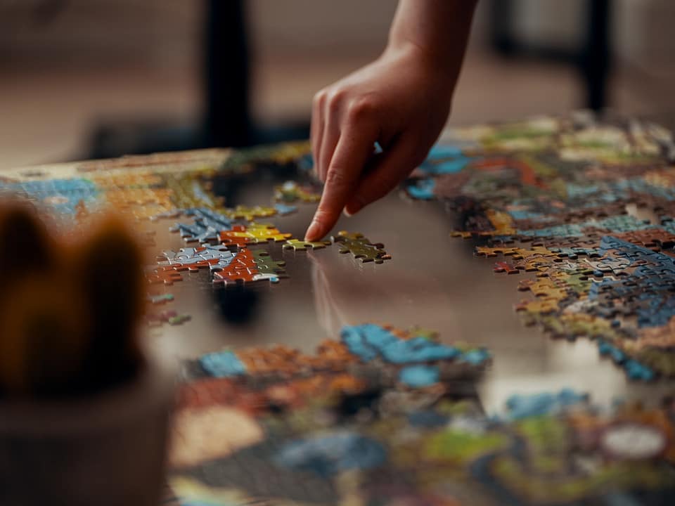 A hand pointing to a puzzle piece, in an incomplete jigsaw puzzle.