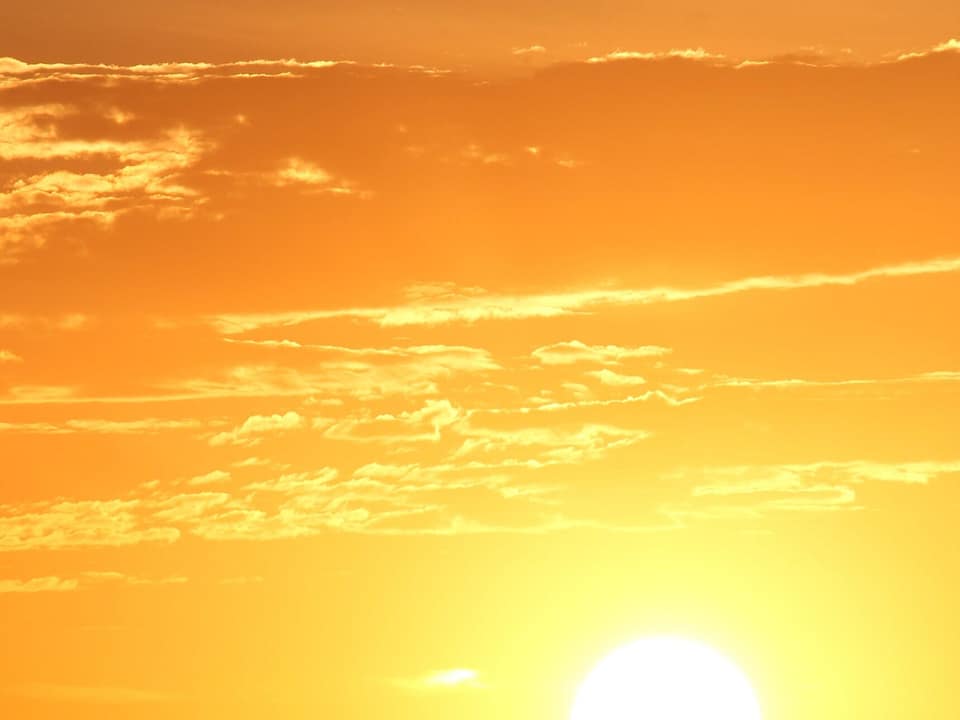 A bright sun, either sunrise or sunset. The sky is orange and yellow, and the sun is barely showing above a piece of land.