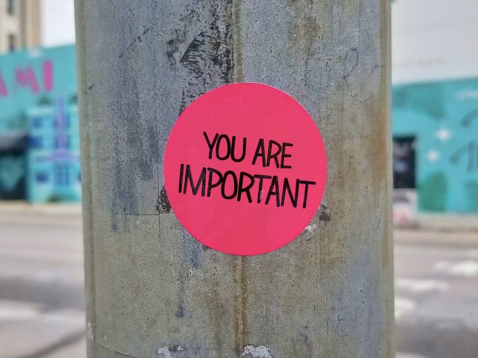 Urbam area. Turquoise painting on a building. There's a pole in the foreground, with a pink sticker that reads, "You are important."