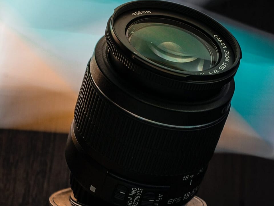A long, black camera lens, standing up, tilted, like the Leaning Tower of Pisa.